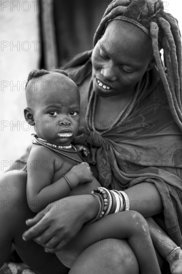 Black and white baby in the arms of a Himba woman, traditional Himba village, Kaokoveld, Kunene, Namibia