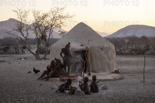 Himba woman and children sitting in front of a hut, sunrise, traditional Himba village, Kaokoveld, Kunene, Namibia