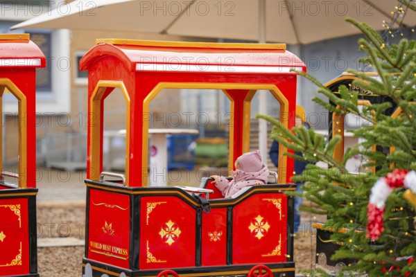 A child sits on a red miniature train next to a Christmas tree at a market, Sindelfingen, Böblingen district, Germany