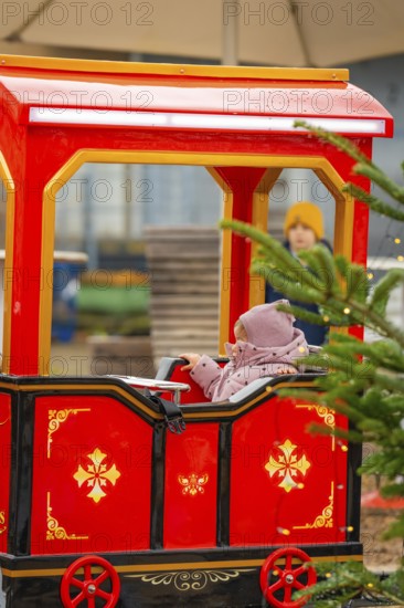 Little girl sitting on a red toy train at a Christmas market, Sindelfingen, Böblingen district, Germany
