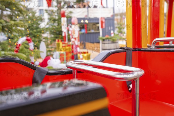 Close-up of a Christmas carousel ride with red and yellow seats in front of a decorated tree, Sindelfingen, Böblingen district, Germany