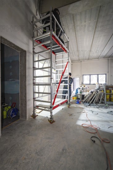 High scaffolding in an unfinished interior with a worker, construction in progress, electrician, new building, Germany