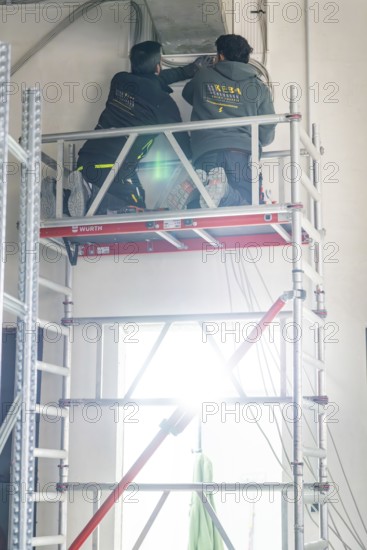 Two workers standing on scaffolding and working on a ceiling with strong light, electrician, new building, Germany
