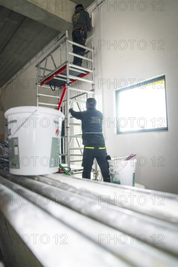 Two workers on scaffolding work on the wall, buckets and pipes are in the foreground, electrician, new building, Germany