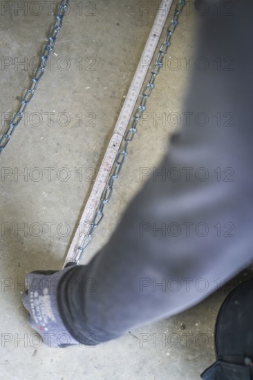 A hand pulls on a chain lying on the ground next to a tape measure, electrician, new building, Germany