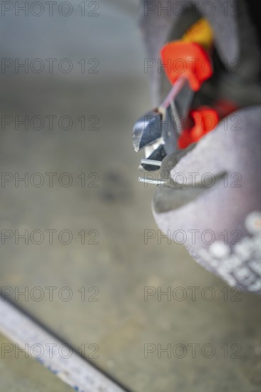 Close-up of pliers cutting wire while a glove-clad hand holds them, electrician, Neubau, Germany