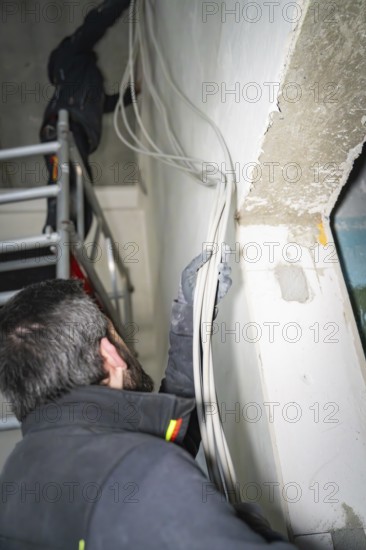 A worker is laying cables along a wall in a renovated room, electrician, new building, Germany