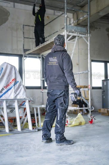 A worker on scaffolding works in a construction site, another worker standing next door, electrician, new building, Germany