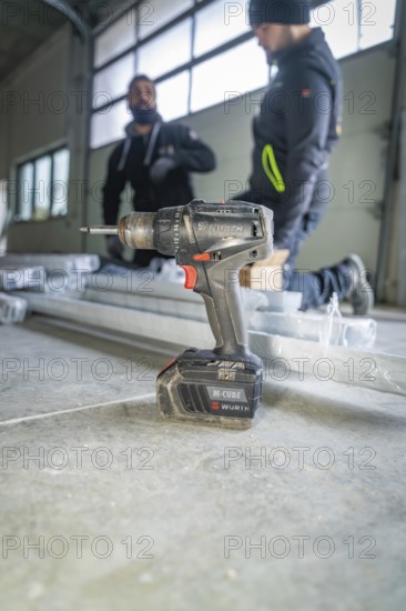 A drill is in the foreground while two workers work in the background, electrician, Neubau, Germany