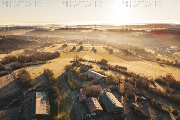 Wide view of fields and farm in fog with gentle sunrise in the distance, Gechingen, Hecken and GÃ¤u region, Calw district, Germany
