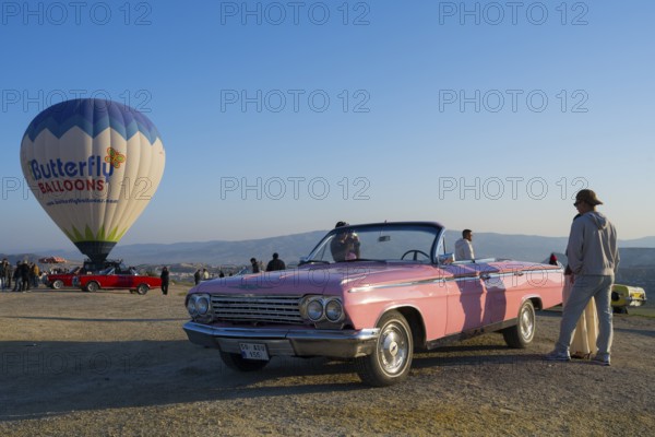 Person standing next to pink cabriolet and hot air balloon under clear fresh morning sky, Chevrolet, Göreme National Park, Göreme Tarihî Millî Park, Nevsehir Province, Nevsehir, Cappadocia, Cappadocia, Central Anatolia, Turkey