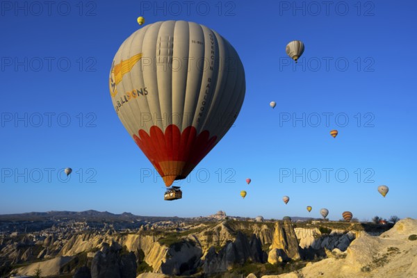 Large hot air balloon soars over a vast, rocky landscape under clear skies, Göreme National Park, Göreme Tarihî Millî Park, Nevsehir Province, NevÅŸehir, Cappadocia, Cappadocia, Central Anatolia, Turkey