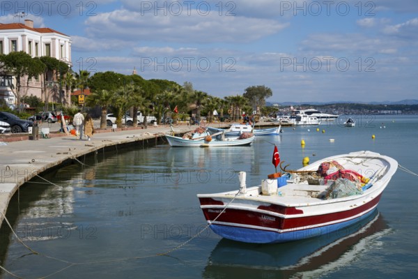 Small boats lie quietly in the harbor on a paved coast under blue sky, Alibey, Alibey Adasi Island, Cunda Adasi, Ayvalik Islands, Ayvalik, Aegean Sea, Turkey