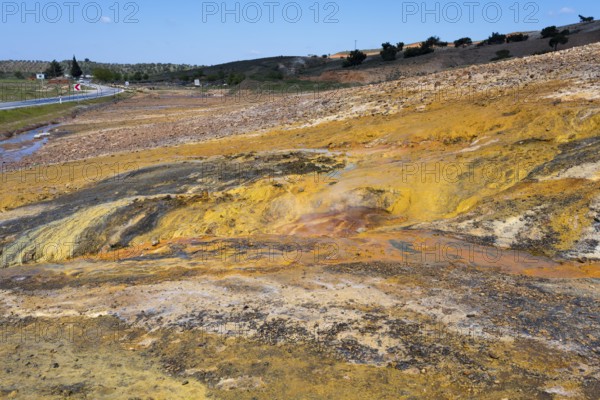 A colorful natural landscape with yellow and orange rocks next to a road under a blue sky, geothermal area, rainbow rocks Tuzla, AyvacÄ±k, Ayvacik, Ã‡anakkale, Canakkale, Turkey