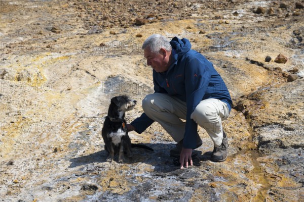 Man playing with dog in a rocky, natural environment, dressed in outdoor clothing, dog and man looking at each other