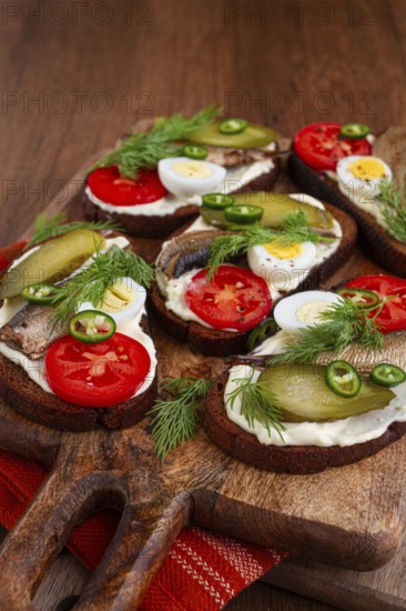 Sandwiches on rye bread with sprats, quail eggs, fresh tomatoes and pickled cucumber, on a wooden board, appetizer, breakfast