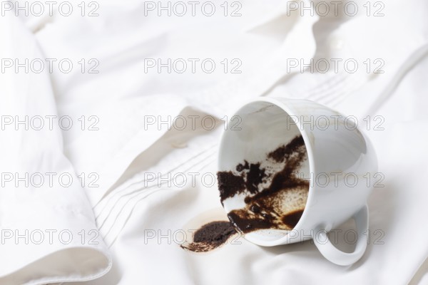 A white cup with the remains of coffee, spilled, lies on a white shirt, there are no people, a soft focus