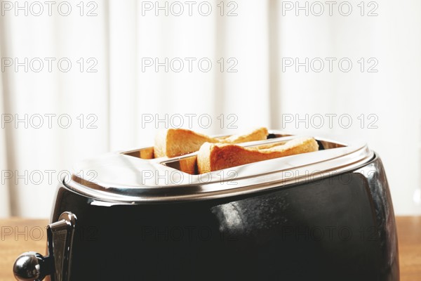 Two slices of bread are toasting in a shiny metal toaster, set on a countertop in a warm kitchen. The soft light suggests a cozy breakfast atmosphere
