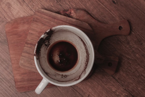 A warm coffee cup sits on a wooden cutting board, showing traces of dark liquid and coffee grounds. This scene captures a moment of relaxation and comfort during a quiet time