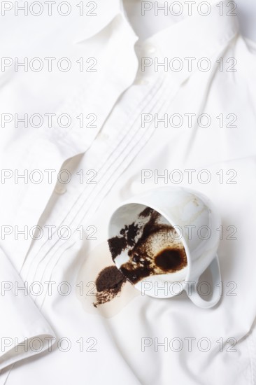 A white cup with the remains of coffee, spilled, lies on a white shirt, there are no people, a soft focus