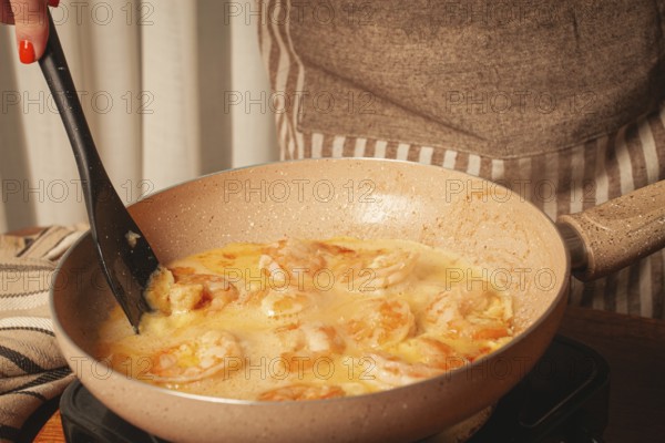 In a cozy kitchen, a person is stirring shrimp in a creamy sauce on the stove. The scene captures the joy of cooking, with warm colors and inviting textures