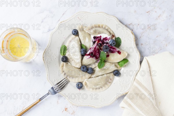 Handmade dumplings filled with sweet ingredients, arranged beautifully on a white plate, topped with berry sauce, fresh blueberries, and mint leaves, ready to enjoy