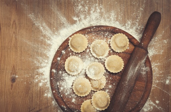 Fresh raw, uncooked ravioli, on a cutting board, with a rolling pin for dough, wooden background, no people