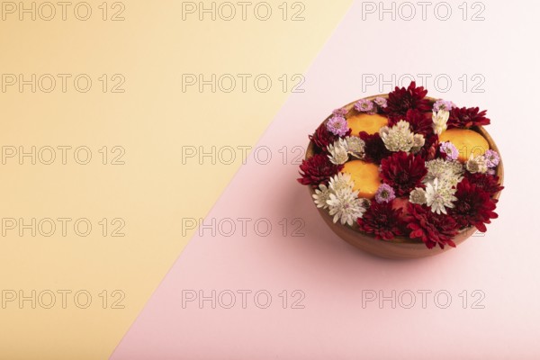 Wooden bowl with carrot slices and red Chrysanthemum flowers, Astrantia flowers, flower salad on pink and orange pastel paper background, side view, copy space, minimalism