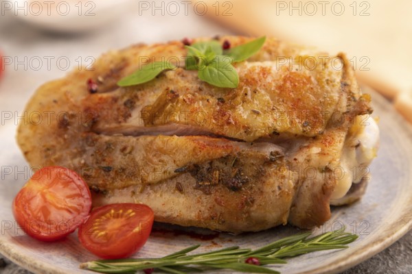 Fried Turkey Thigh with spices and rosemary on plate on brown concrete background and orange linen textile. side view, close up, selective focus