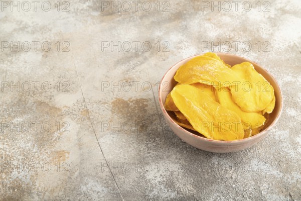 Dried Mango in ceramic bowl on brown concrete background. Side view, copy space. healthy food, minimalism
