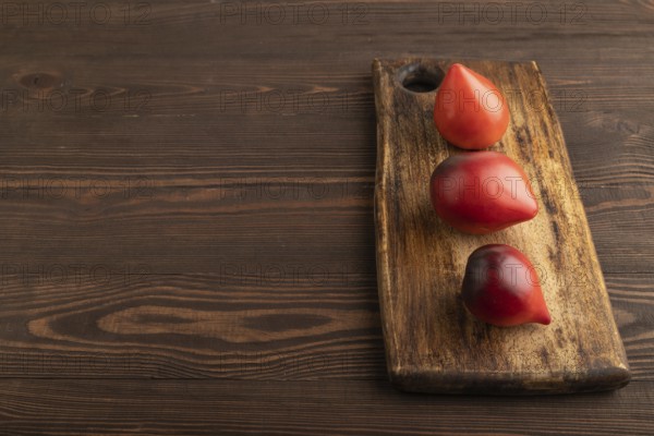 Red Heart shape tomatoes on cutting board on brown wooden background. Side view, copy space. healthy food, vegetable, minimalism