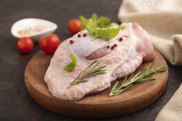 Raw Turkey Thigh with spices and rosemary on cutting board on black concrete background and linen textile. side view, close up, selective focus