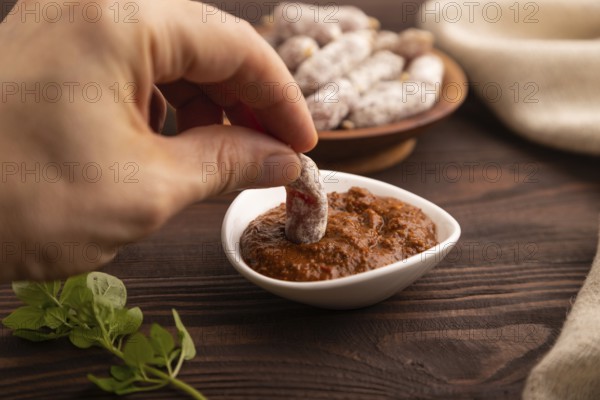 Small smoked Chicken sausages in wooden bowl with hand on brown wooden background and linen textile. side view, close up, selective focus