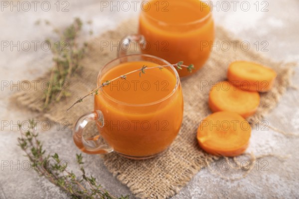 Two glasses with carrot juice, on brown concrete background and linen textile. Diet, healthy eating concept. side view, close up, minimalism, selective focus