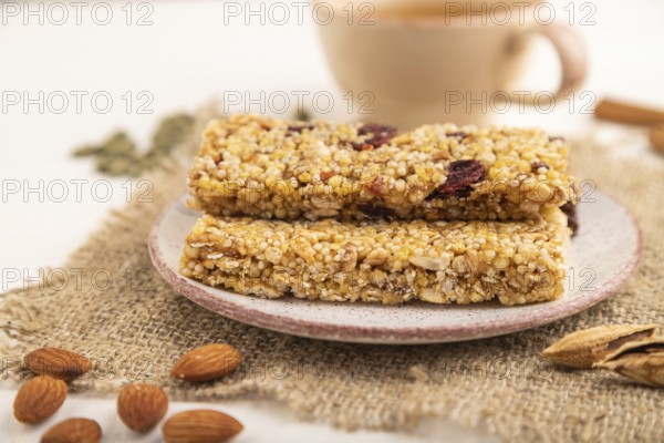 Granola bars with caramel, nuts, flakes in ceramic plate on white wooden background, beige linen napkin, cup of green tea. Side view, close up, selective focus