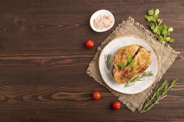 Fried Turkey Thigh with spices and rosemary on plate on brown wooden background and linen textile. top view, flat lay, copy space
