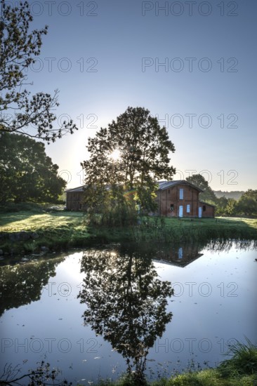 Manor with historic stable and pond, from 1923, in backlight with sun star, Gut Othenstorf, Mecklenburg-Western Pomerania, Germany