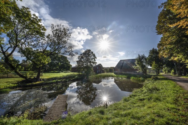Manor with historic stables and pond, from 1923, in backlight with sun star, Gut Othenstorf, Mecklenburg-Western Pomerania, Germany