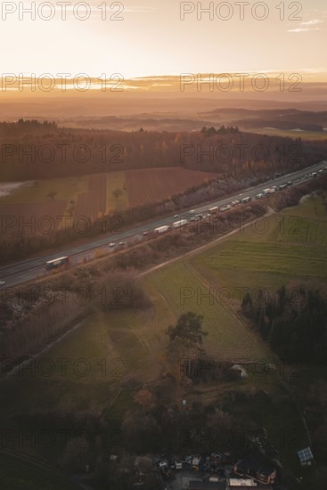 Aerial view of a motorway surrounded by fields and forests as the orange sunset colors the sky, A8 motorway, Germany