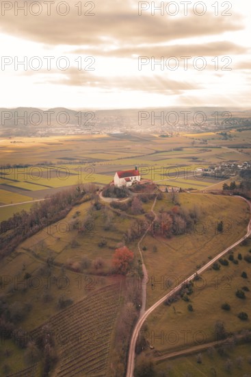 A red church roof on a hill with a view of vast fields under a cloud cover, Wurmlinger Chapel, Rottenburg am Neckar, Germany