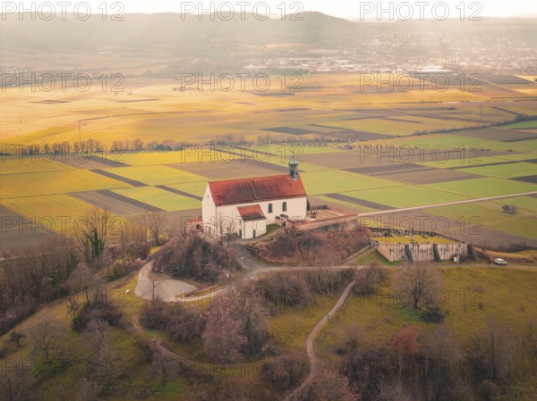 A church with a red roof towers over a vast mosaic of fields in sunlight, Wurmlingen Chapel, Rottenburg am Neckar, Germany