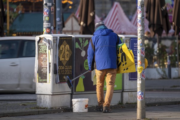 Man sticks posters to electrical boxes near Alexanderplatz, Berlin, Germany