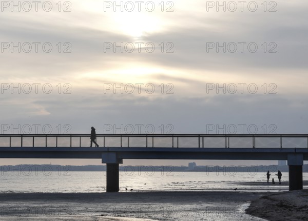 Silhouettes of people on and under a pier, low tide, wave and ripple patterns in wet sand, sunrise, Scharbeutz, 29.11.2025, Scharbeutz, Schleswig-Holstein, Germany