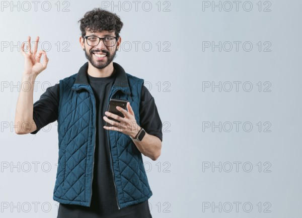 Attractive man in glasses holding phone gesturing OK. Smiling handsome man holding phone and gesturing OK, isolated