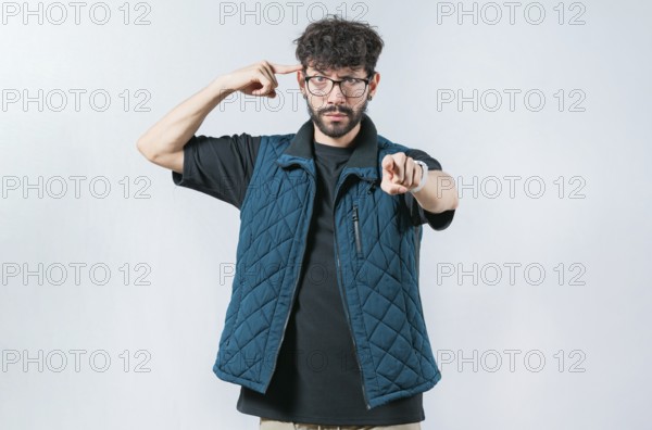 Annoyed bossy man with beard twirling finger to temple pointing finger at camera