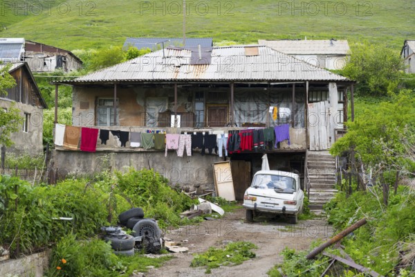 Rural house with clothesline and old car nestled in green landscape with hills, poor house in Semyonovka, Gegharkunik province, Armenia
