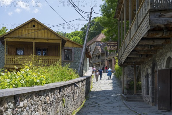 Village street lined with old buildings with wooden verandas flanked by green vegetation under a clear sky, Old Town, Sharambeyan Street, Dilijan, Delijan, Delijan, Tavush Province, Armenia