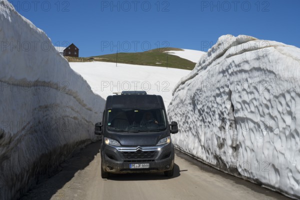 A van drives through thick snow walls on a mountain road under a blue sky, motorhome, camper on a road in a snowwall on the Goderdzi Pass, Ajara region, Adjara, autonomous republic, Georgia