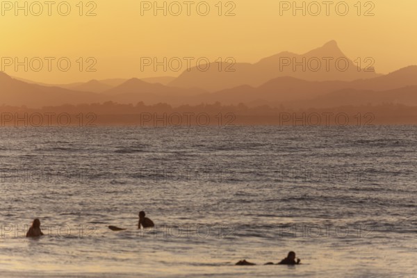 Red sunset on Wategos Beach with surfers in the ocean. Mt. Warning, Wollumbin in the background of the surfing scene. Byron Bay, New South Wales, Australia