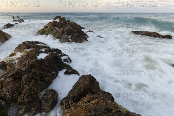 The Cape Byron Lookout at high tide: rocks and anglers in golden light. Byron Bay, New South Wales, Australia